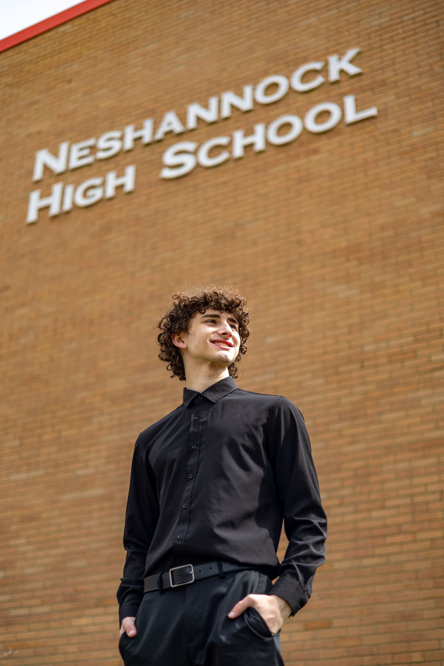 Curly-haired young man in black shirt posing outside Neshannock High School.