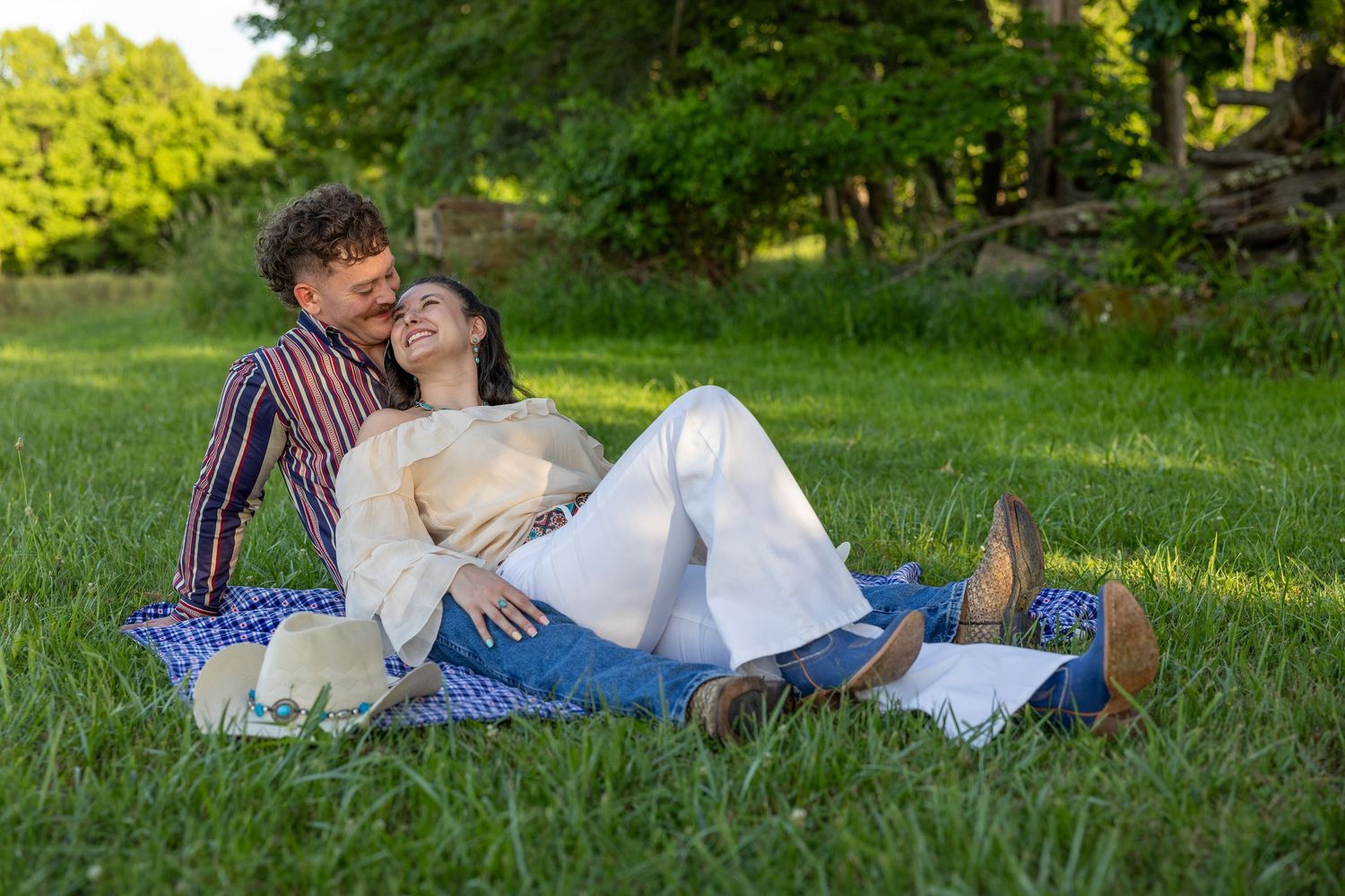 Couple relaxing on a picnic blanket in lush green grass, sharing a tender moment.