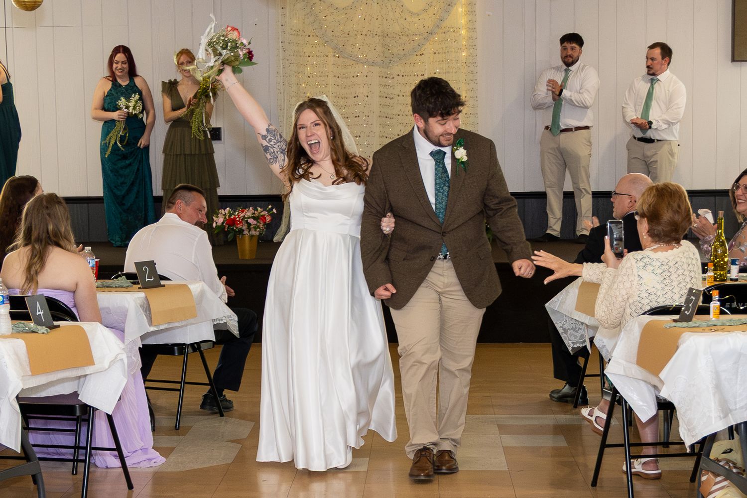 Bride and groom making grand entrance at wedding reception as guests cheer and celebrate.