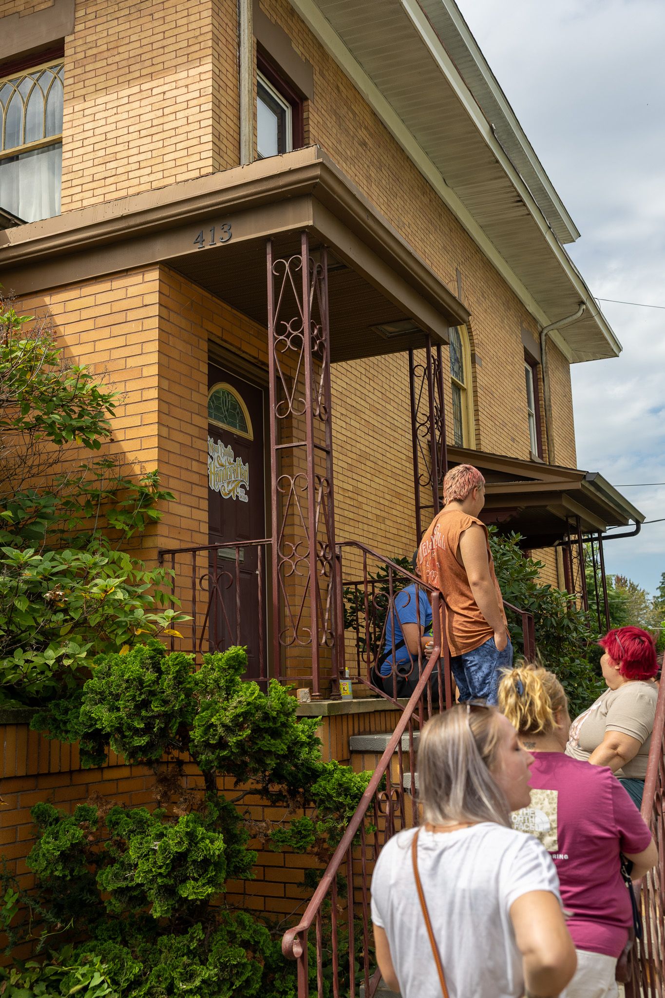 Group of people touring a brick two-story home at number 419, waiting on steps to enter the front porch.