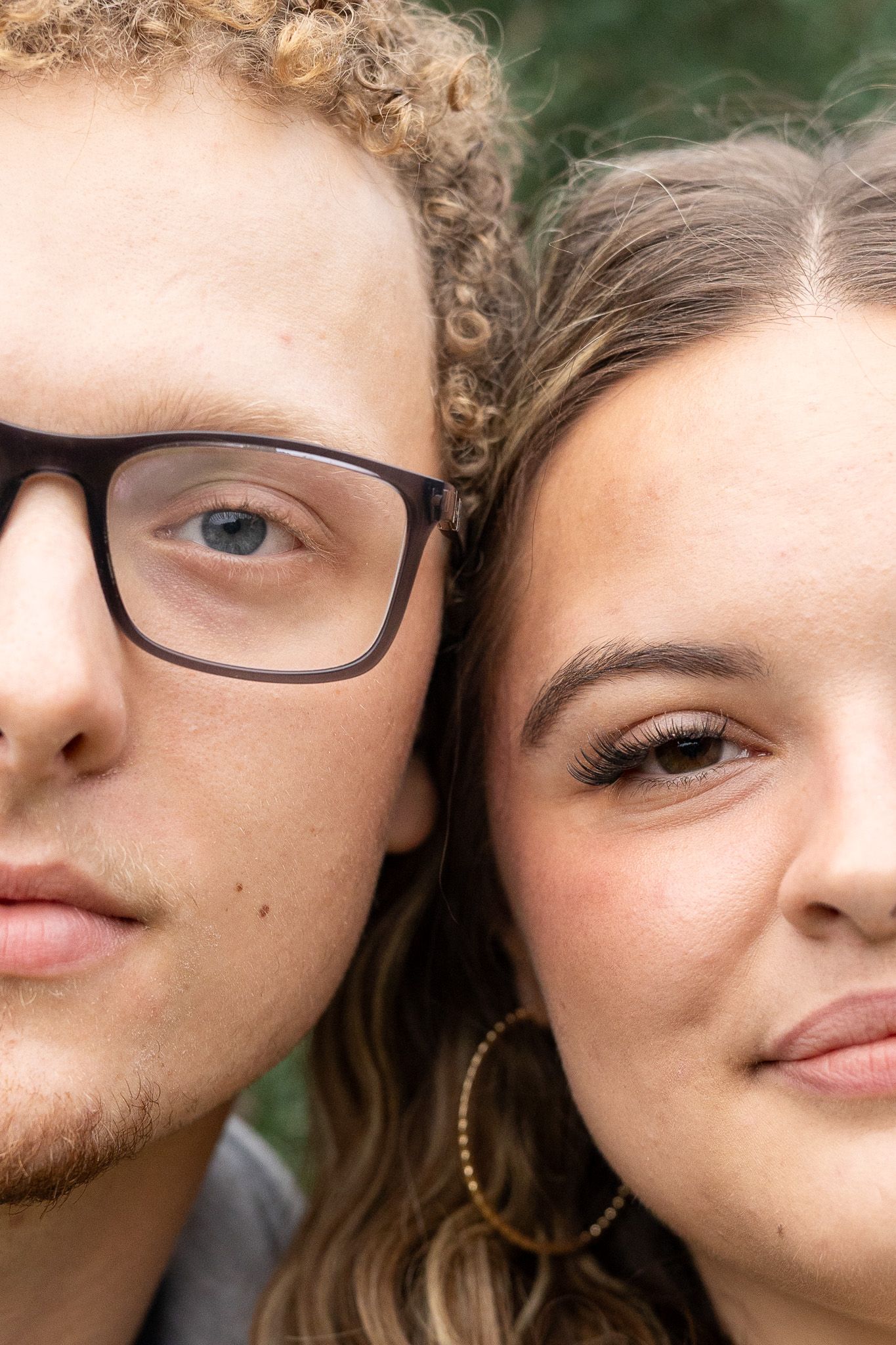 Close-up portrait of a young couple cheek to cheek, man wearing black glasses, woman with hoop earrings, smiling softly.