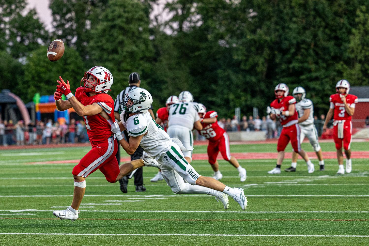 Red team player attempts to catch a football while being defended by a green team player during a high school football game.