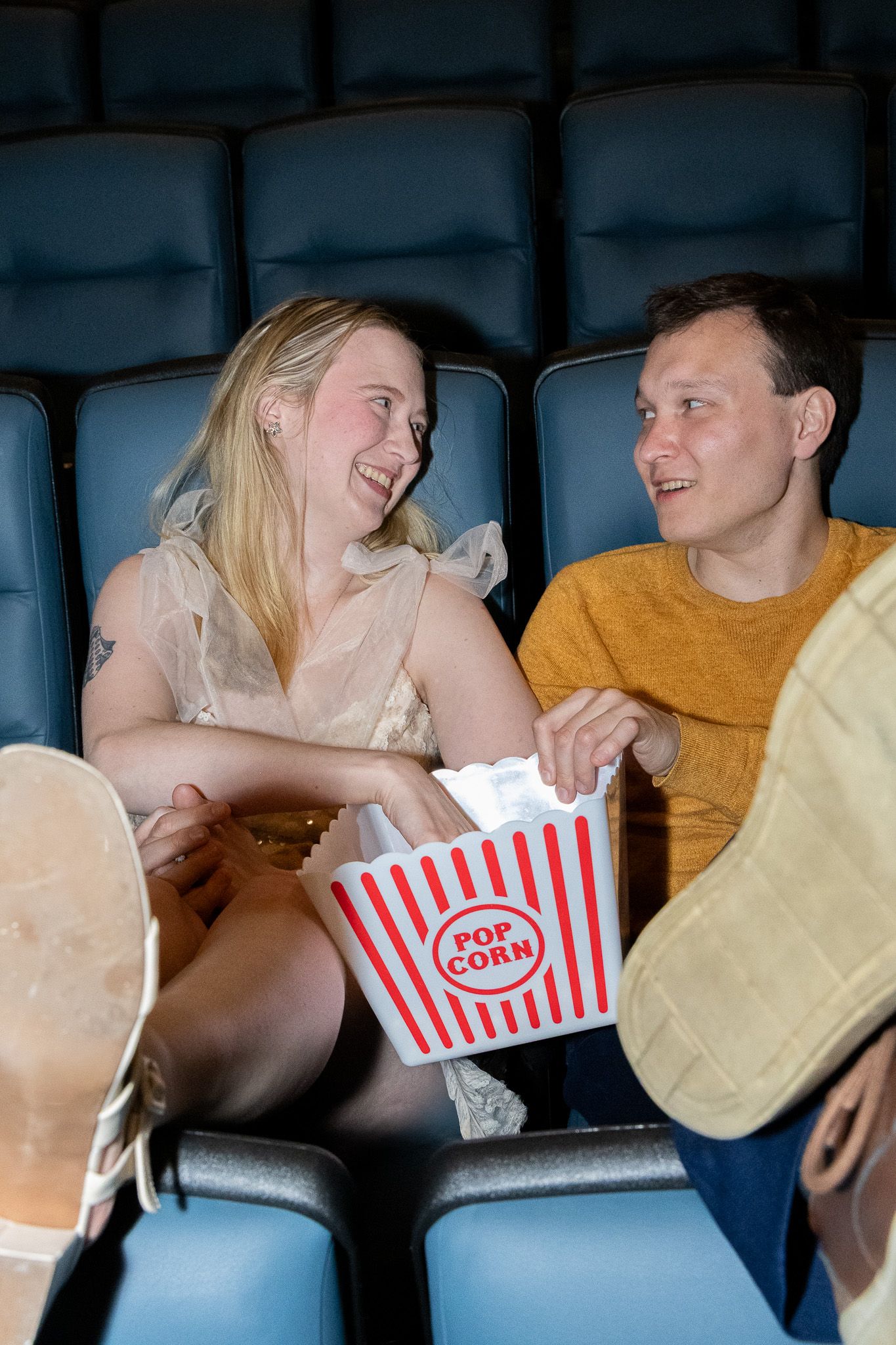 Happy couple sharing popcorn box and laughing together at the cinema.