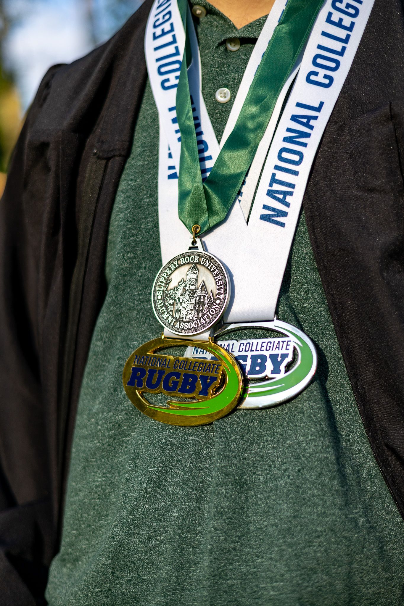 Close-up of a person wearing two National Collegiate Rugby medals on green and white lanyards.