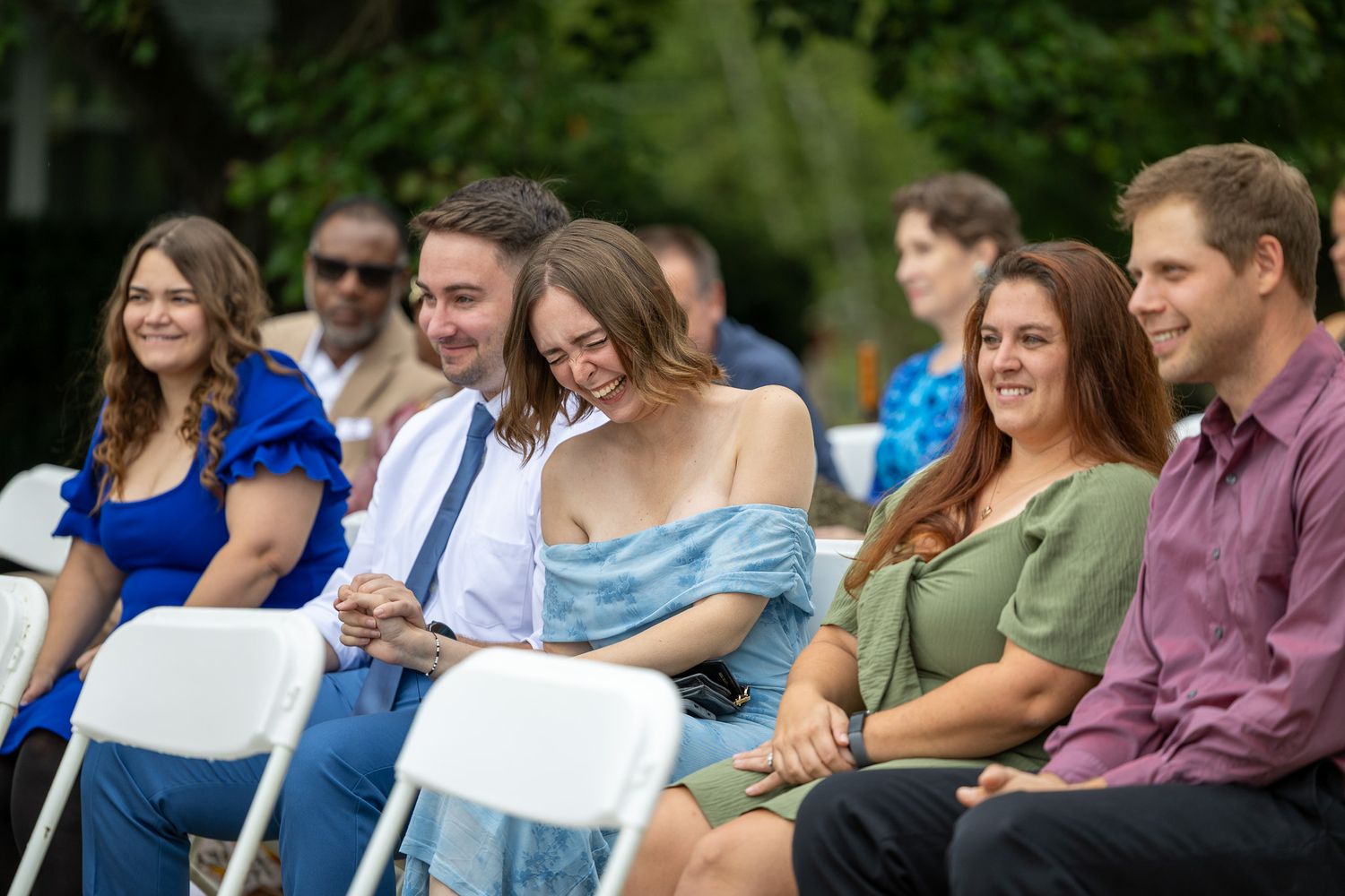 Group of smiling young adults seated outdoors at a casual event, enjoying a sunny day in colorful attire.