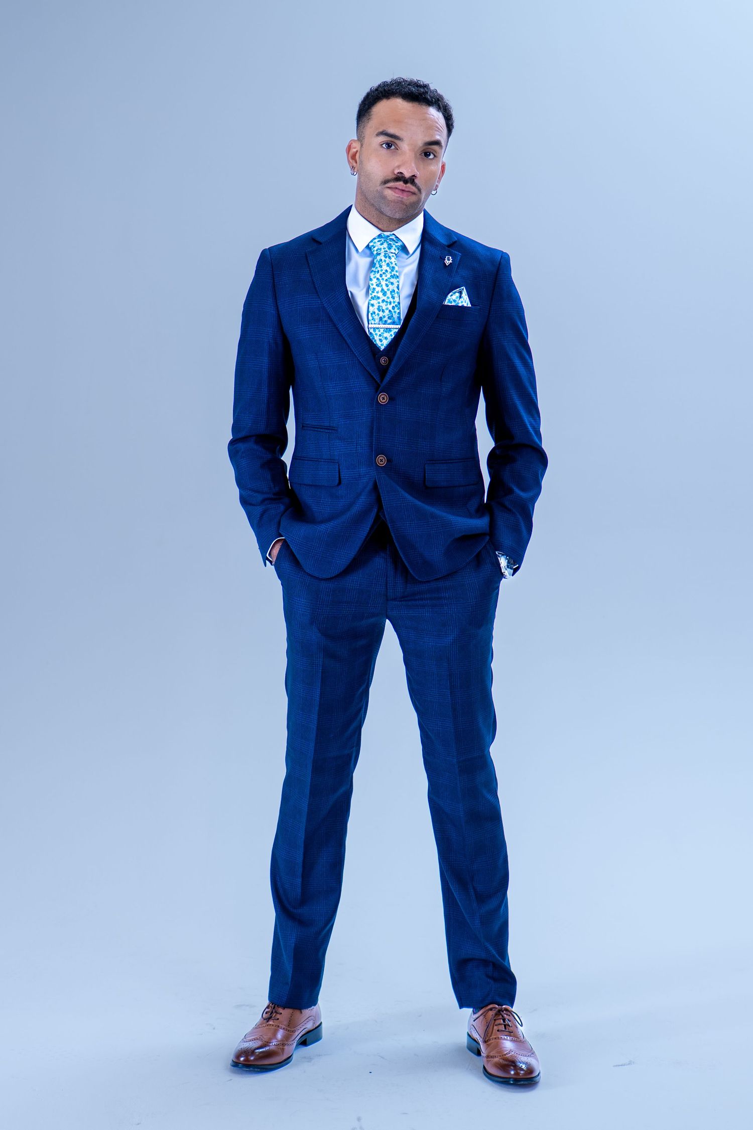 Man in a navy blue three-piece suit with teal tie and pocket square posing in a studio.
