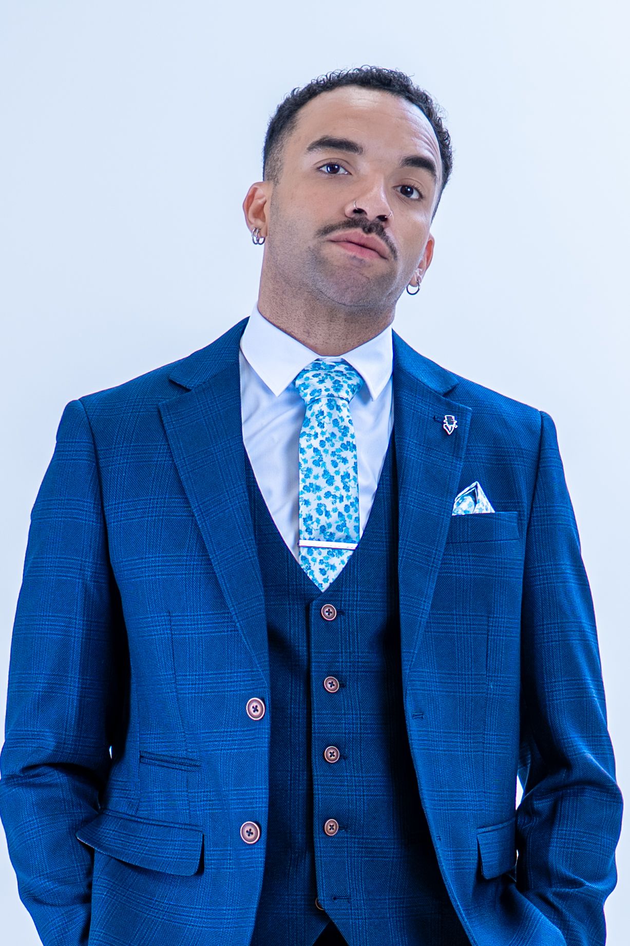 Confident man in navy checked three-piece suit with blue floral tie and pocket square.