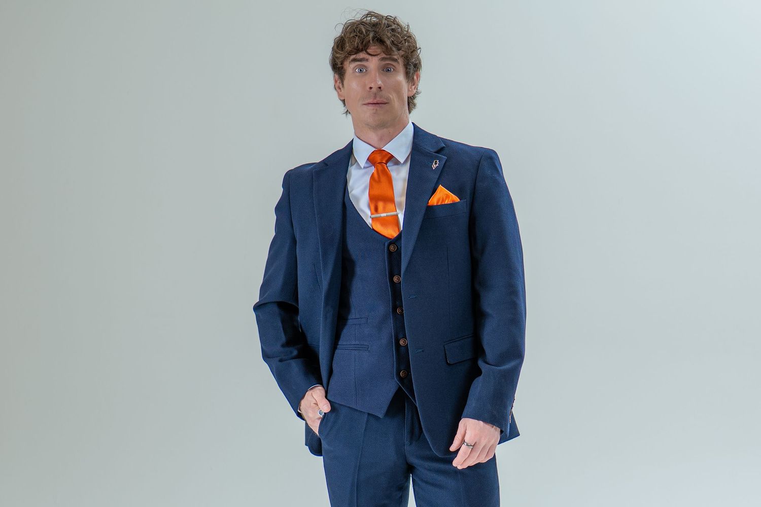 Man in navy blue three-piece suit with bold orange tie and matching pocket square.
