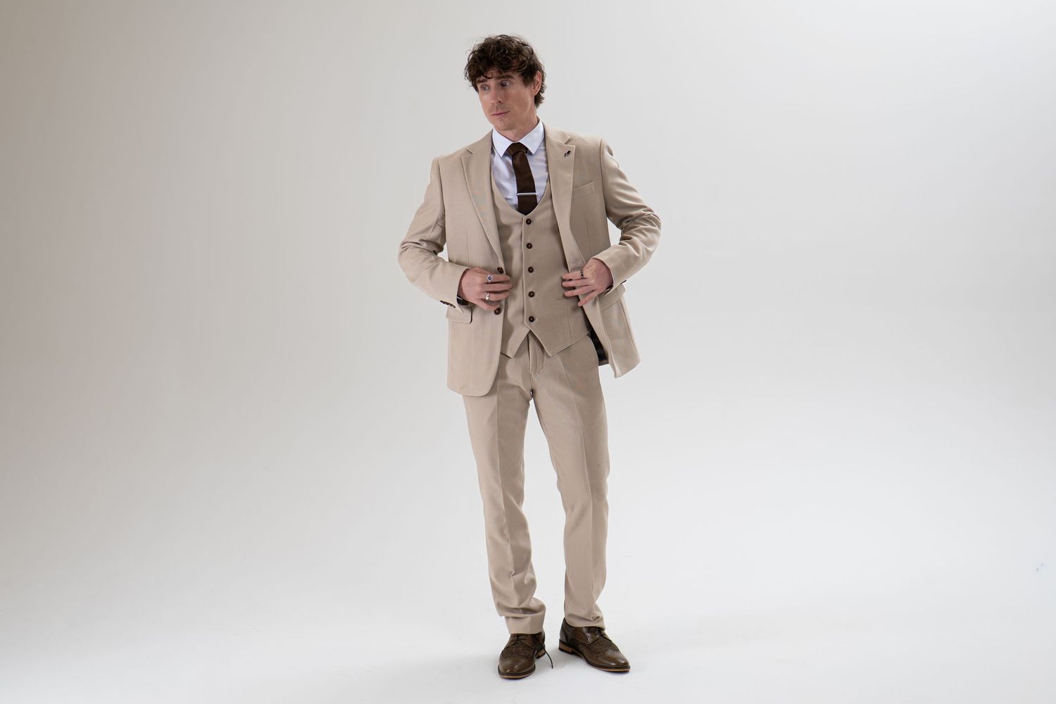Man in beige three-piece suit with hands on hips, full-length studio portrait.