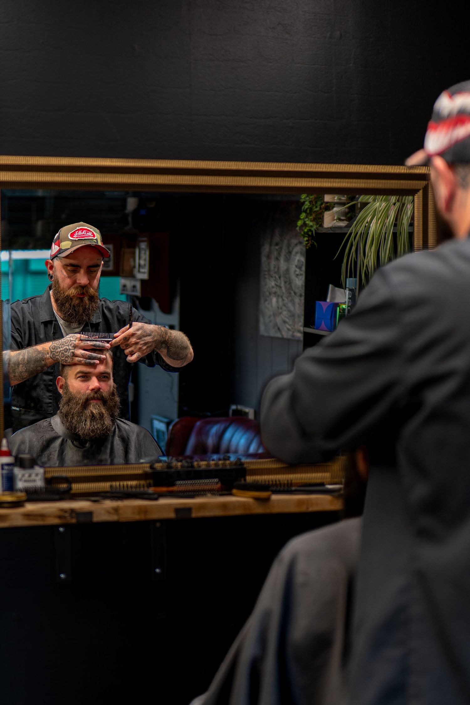 Barber and bearded client reflected in mirror during haircut at stylish barbershop.