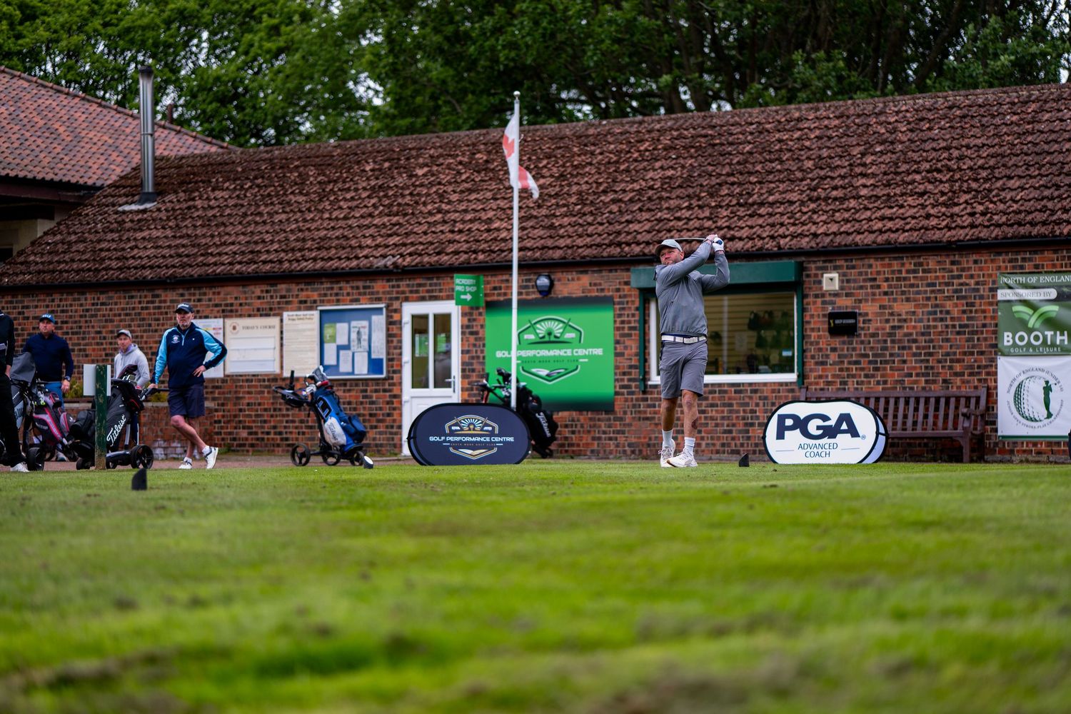 Golfer prepares to tee off at a PGA golf tournament with branded banners on display.