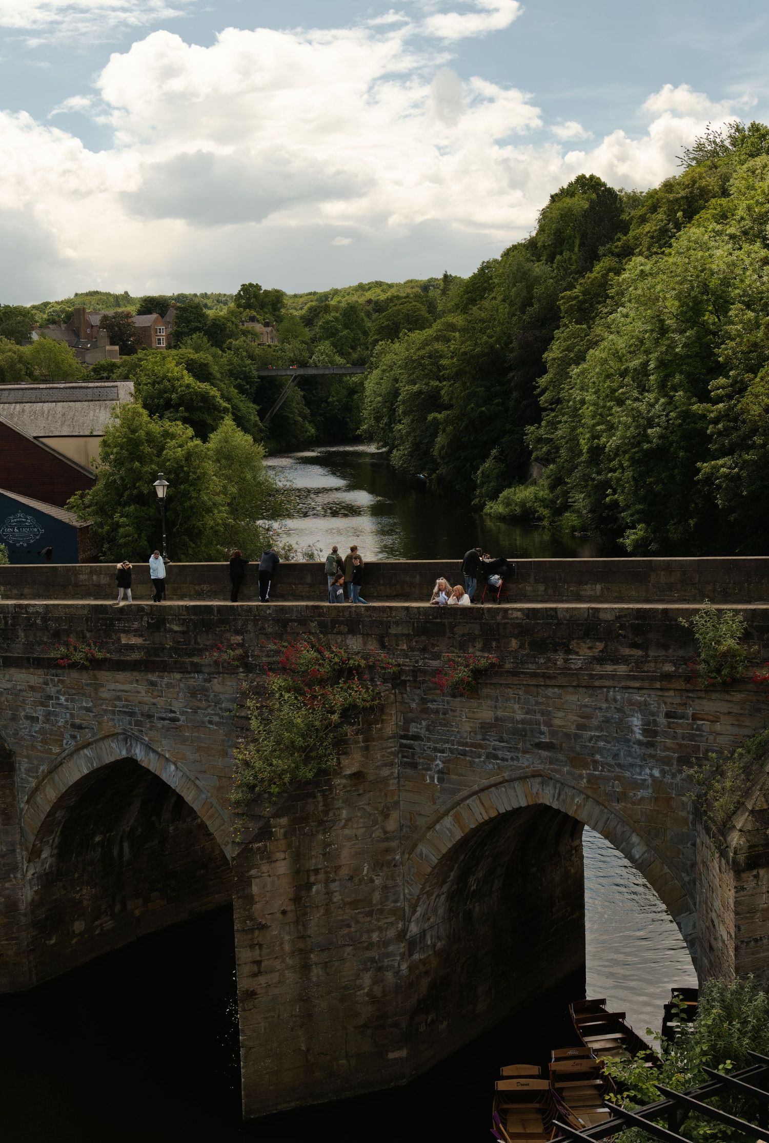 Historic stone arch bridge over river surrounded by dense green trees in Durham.