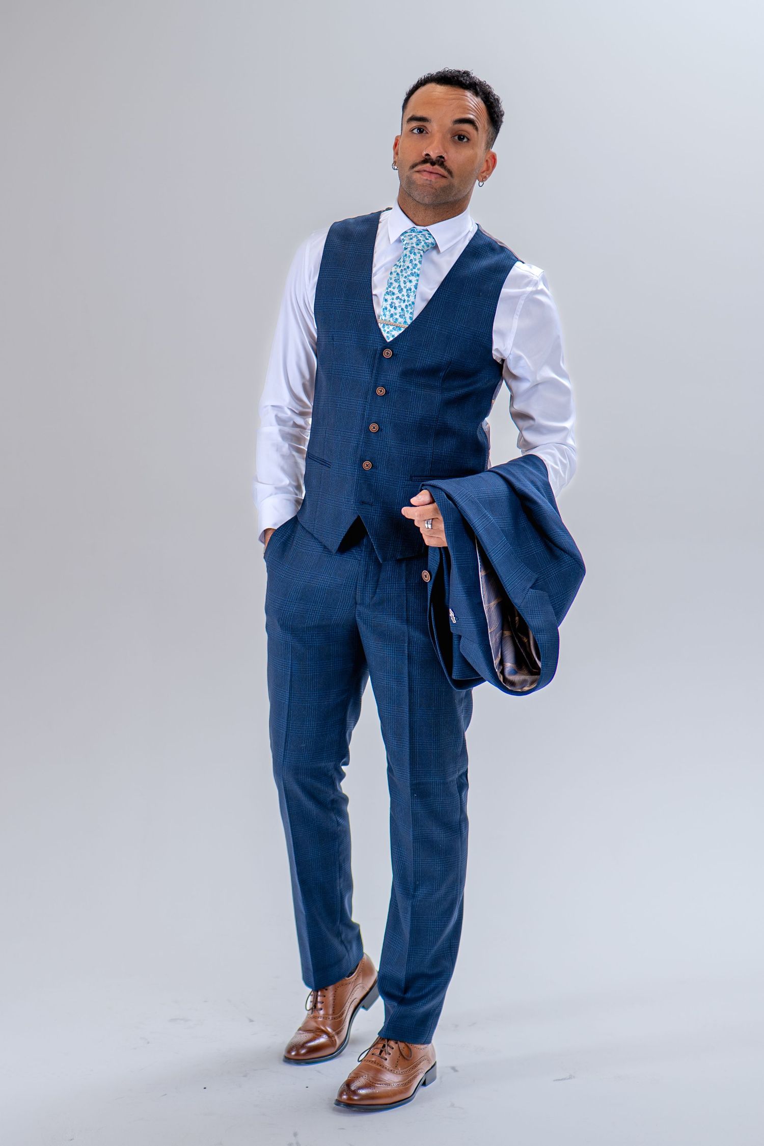 Man holding navy suit jacket over shoulder, wearing matching waistcoat and trousers with blue tie.