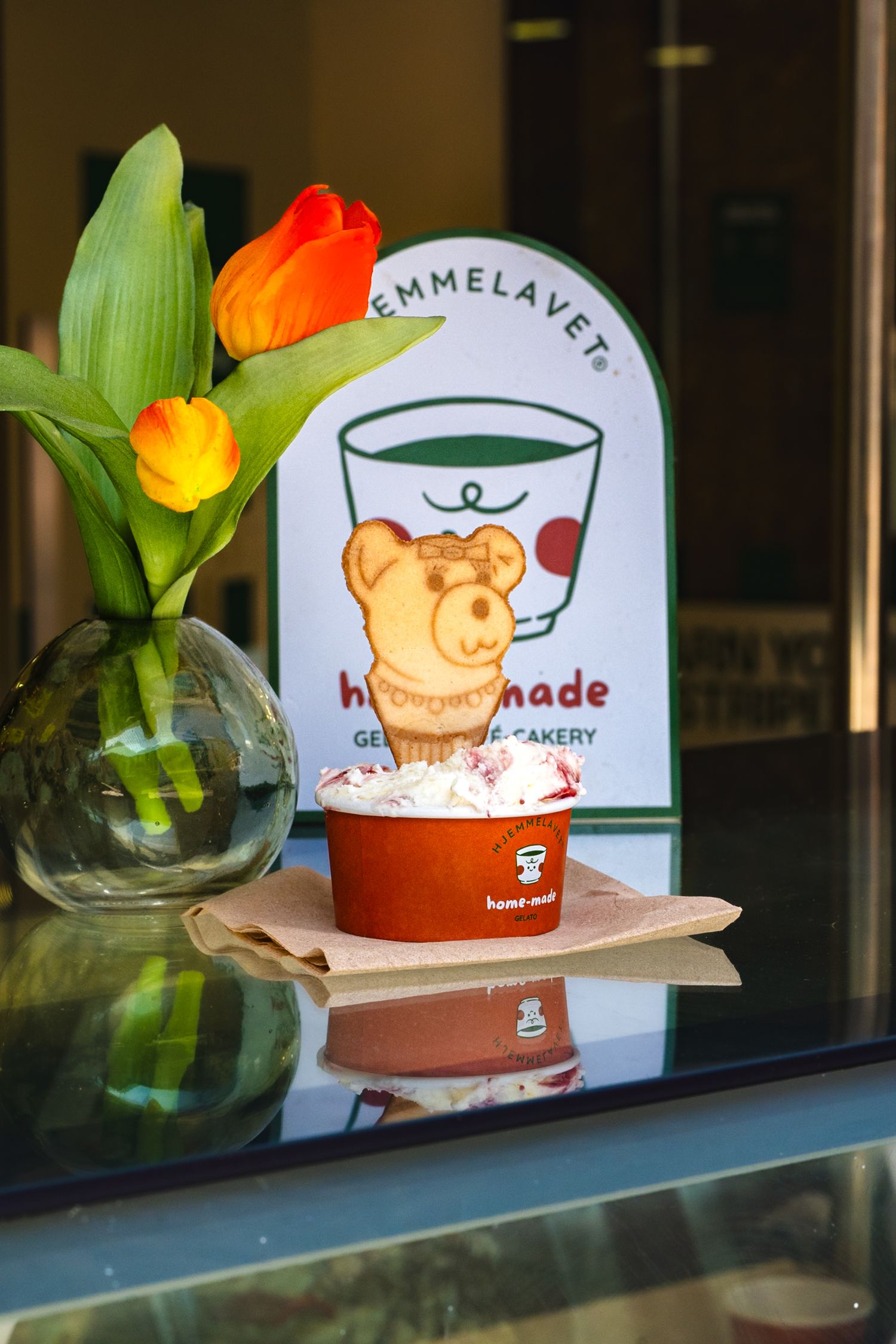 Homemade gelato cup with bear waffle cookie beside orange tulips at Hemmelavet bakery.