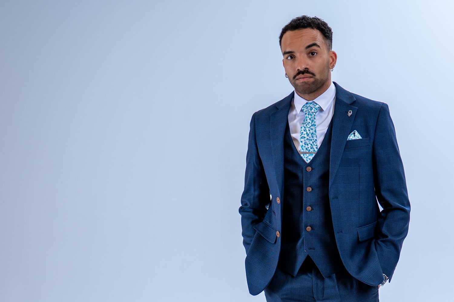 Stylish man in navy blue three-piece suit with floral blue tie and matching pocket square.