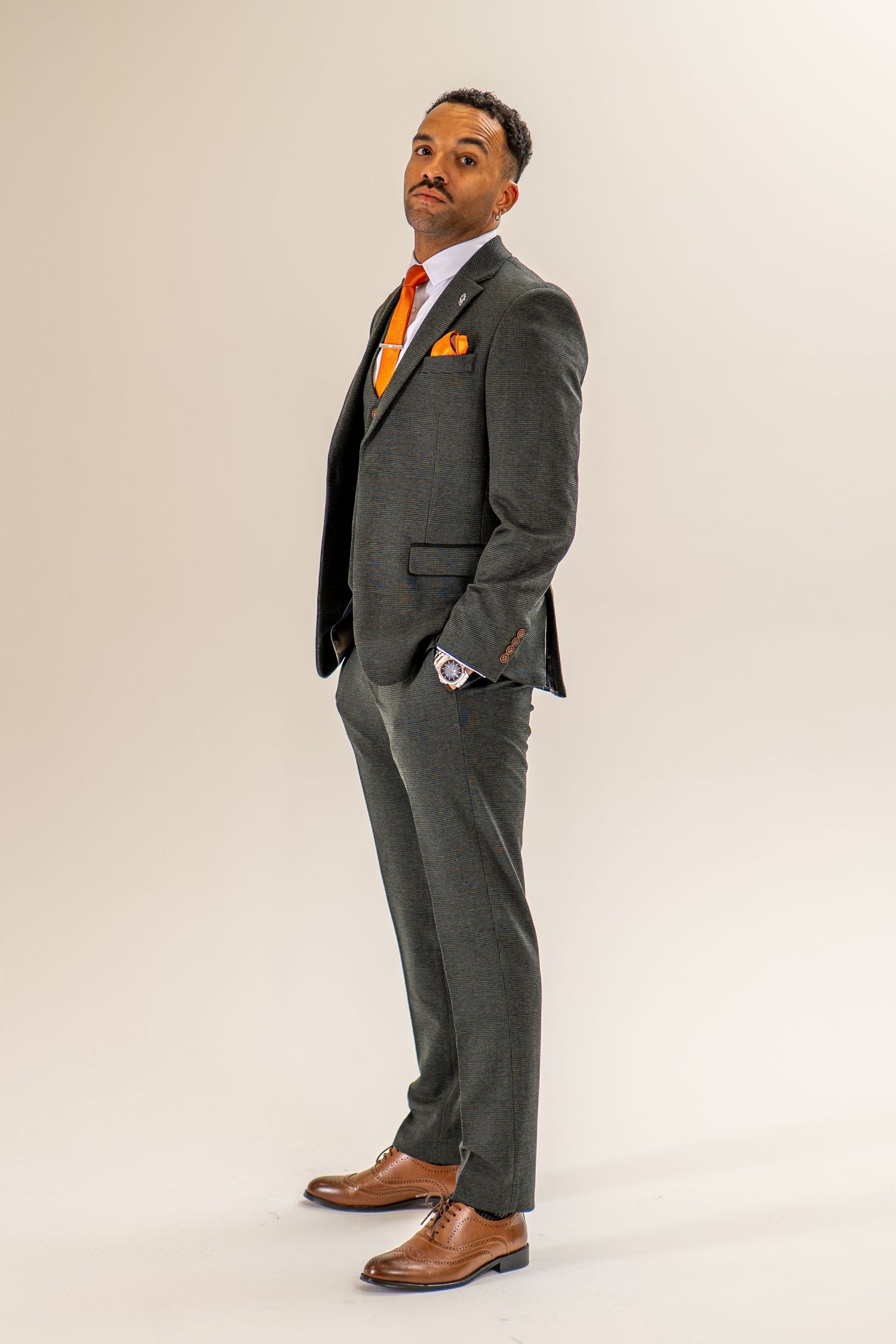 Stylish man posing in charcoal three-piece suit with orange tie and matching pocket square.