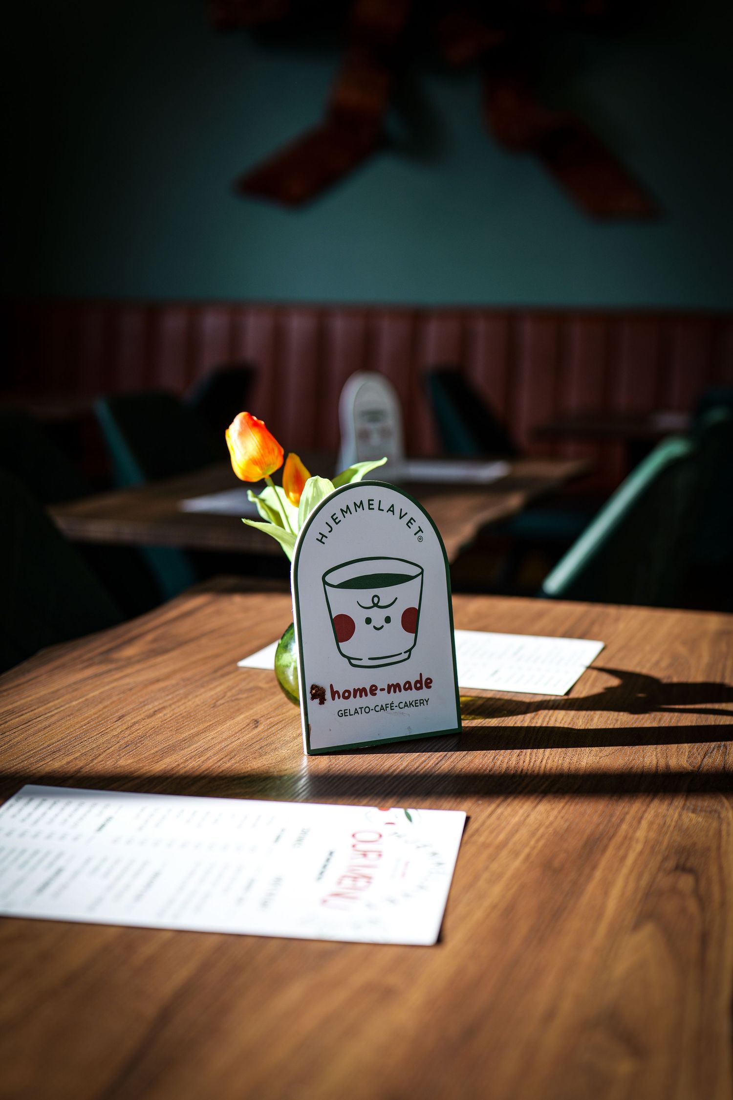 Wooden cafe table with a single orange tulip and home-made gelato cafe candy branded menu holder.