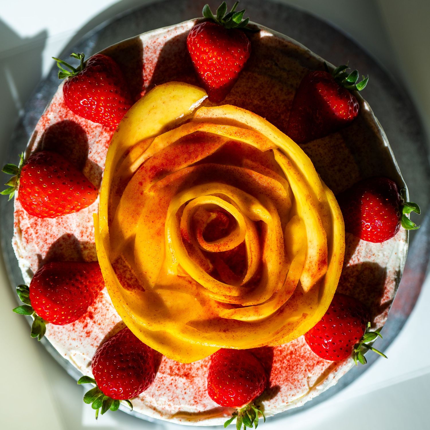 Top view of white cake decorated with mango rose and fresh strawberries.