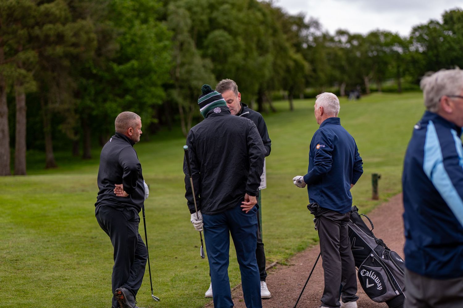 Golfers gather on a lush green golf course fairway discussing strategy during a PGA golf event.