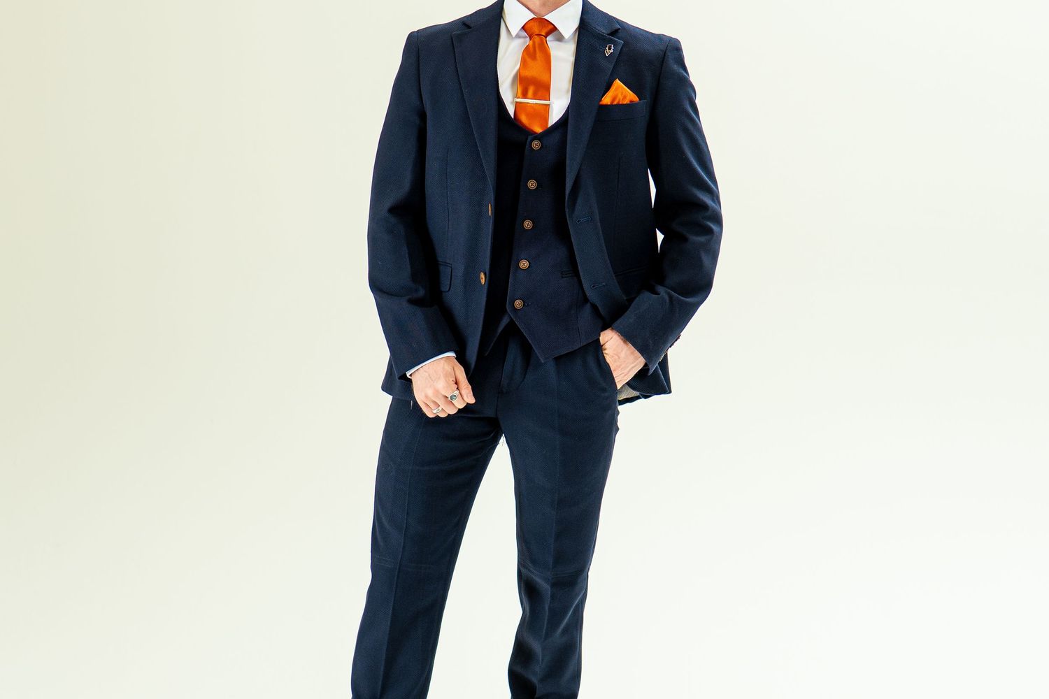 Full-length view of man in navy checked three-piece suit with orange tie and pocket square.
