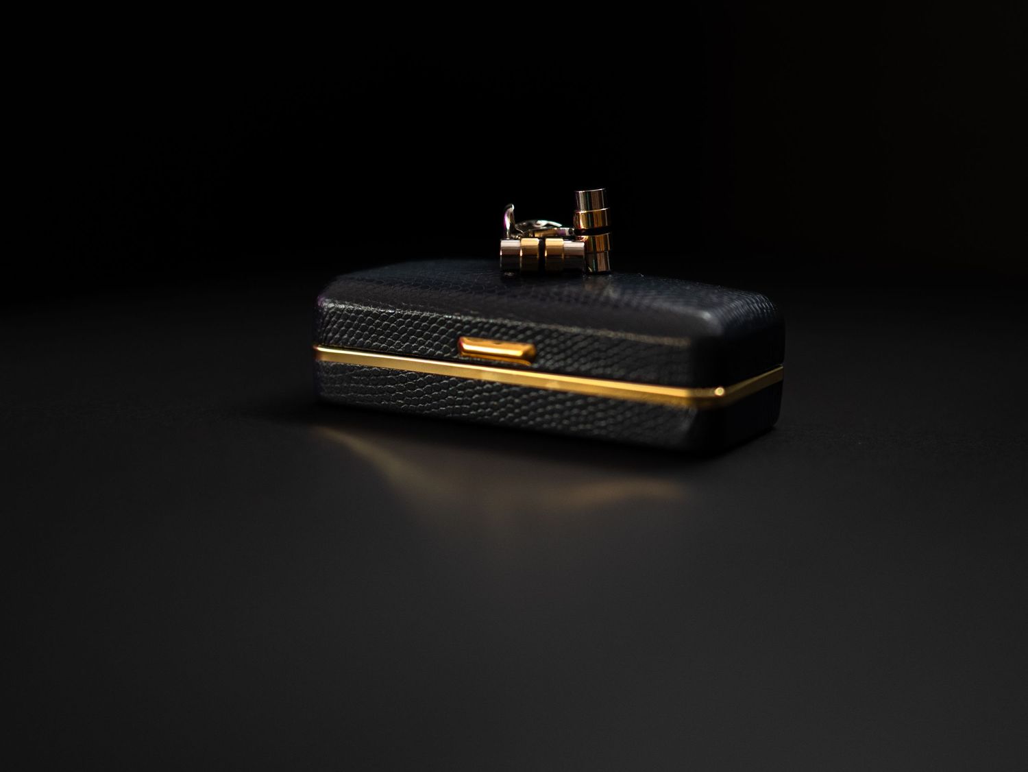 Luxury black textured rectangular jewelry box with gold hardware and clasp on dark background.