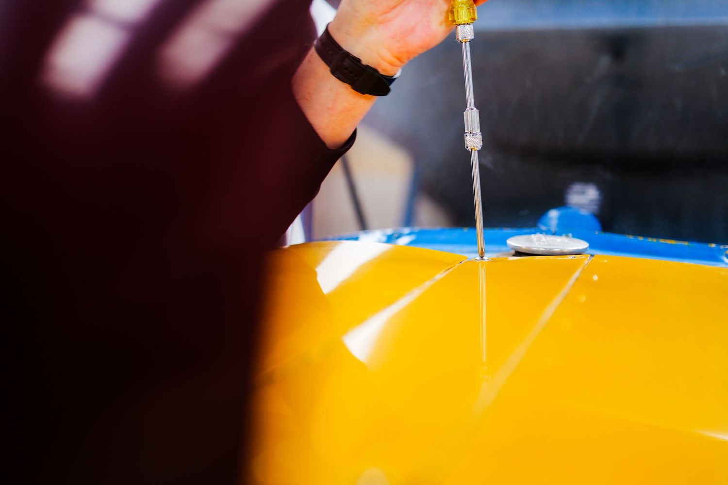 Close-up of a hand using a screwdriver on a yellow aircraft surface during maintenance.