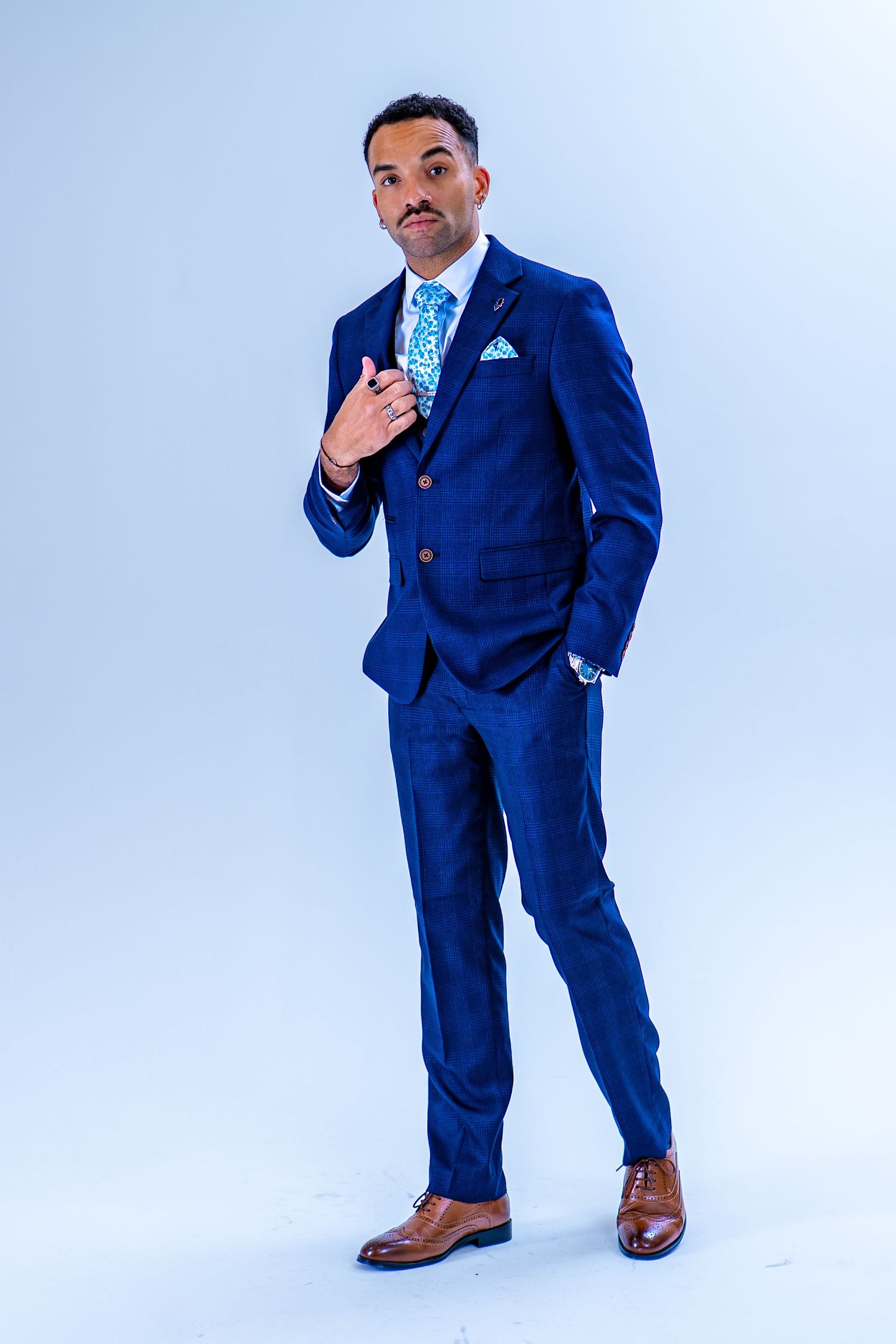 Man in navy blue three-piece suit with light blue tie and pocket square, posing confidently in studio.