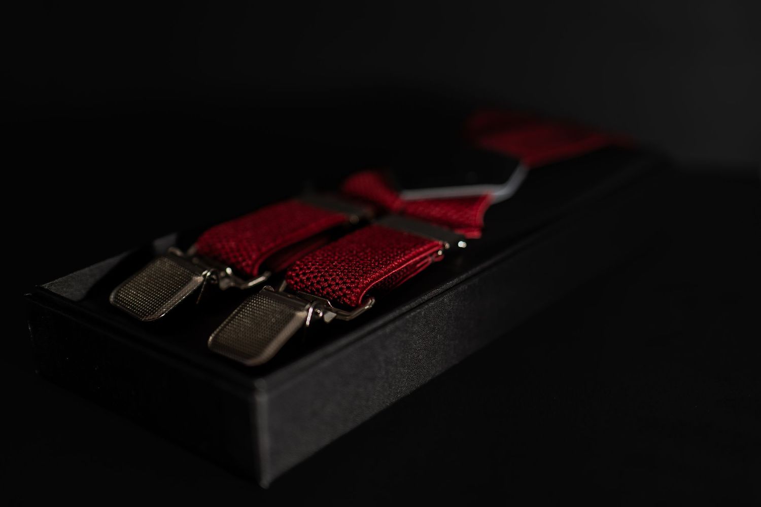Red suspenders with silver clips displayed in a black gift box on a dark background.