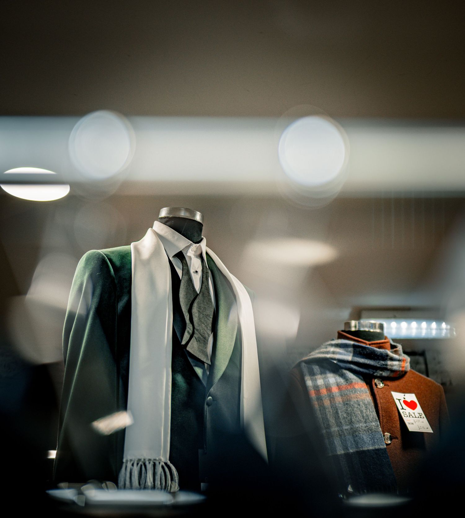 A mannequin wearing a green suit with a white scarf displayed in a softly lit retail clothing store.