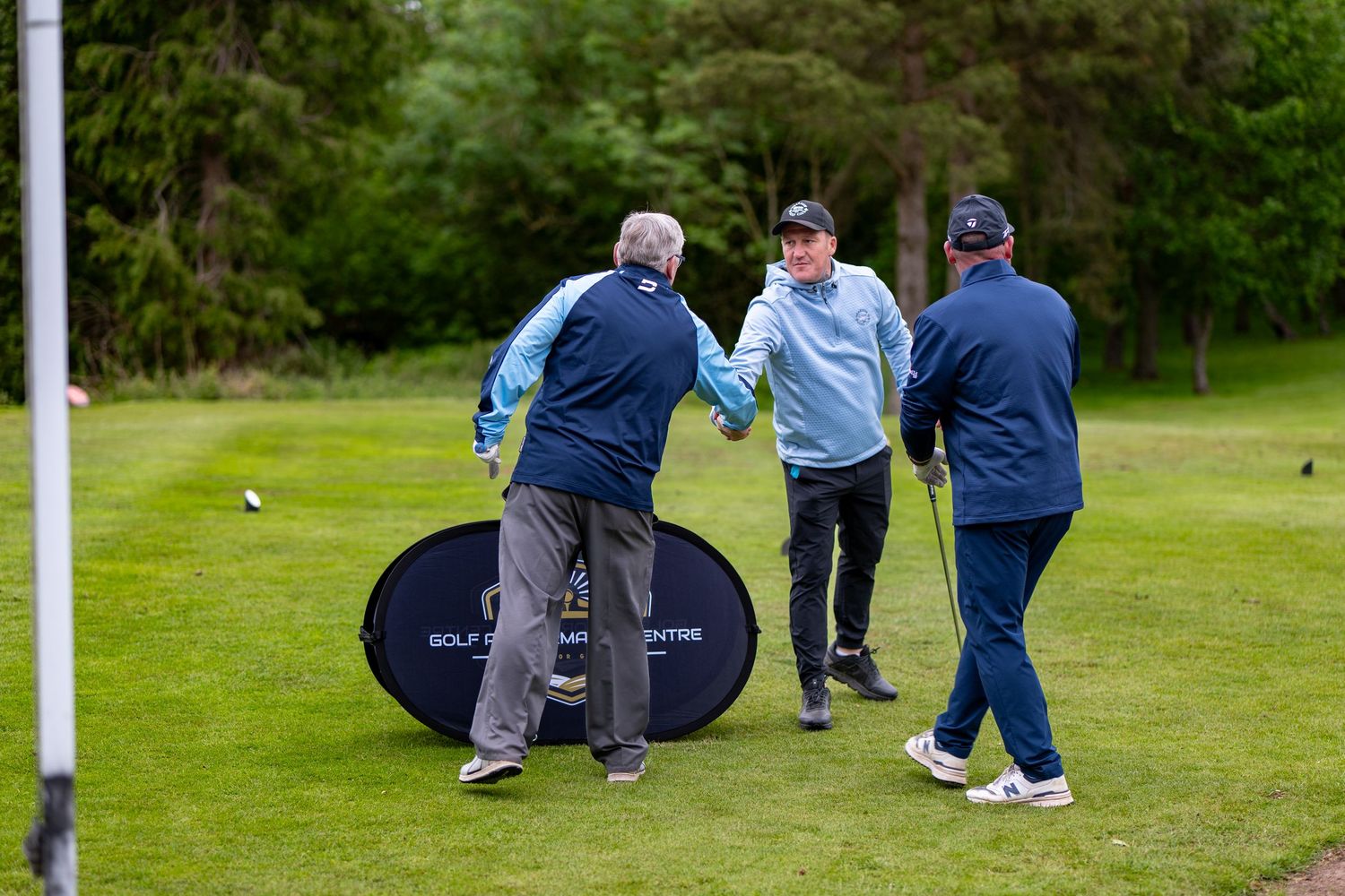 Three golfers greet each other with handshakes on a green golf course fairway.