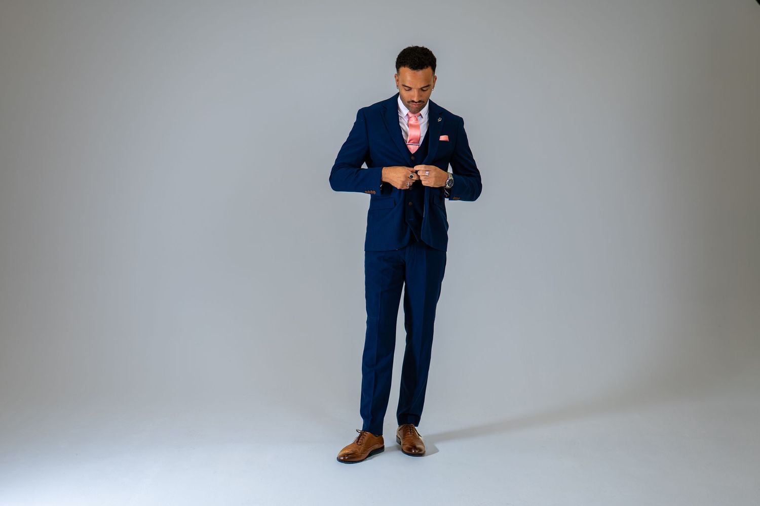Elegant man in navy blue suit with pink tie buttoning jacket in studio setting.
