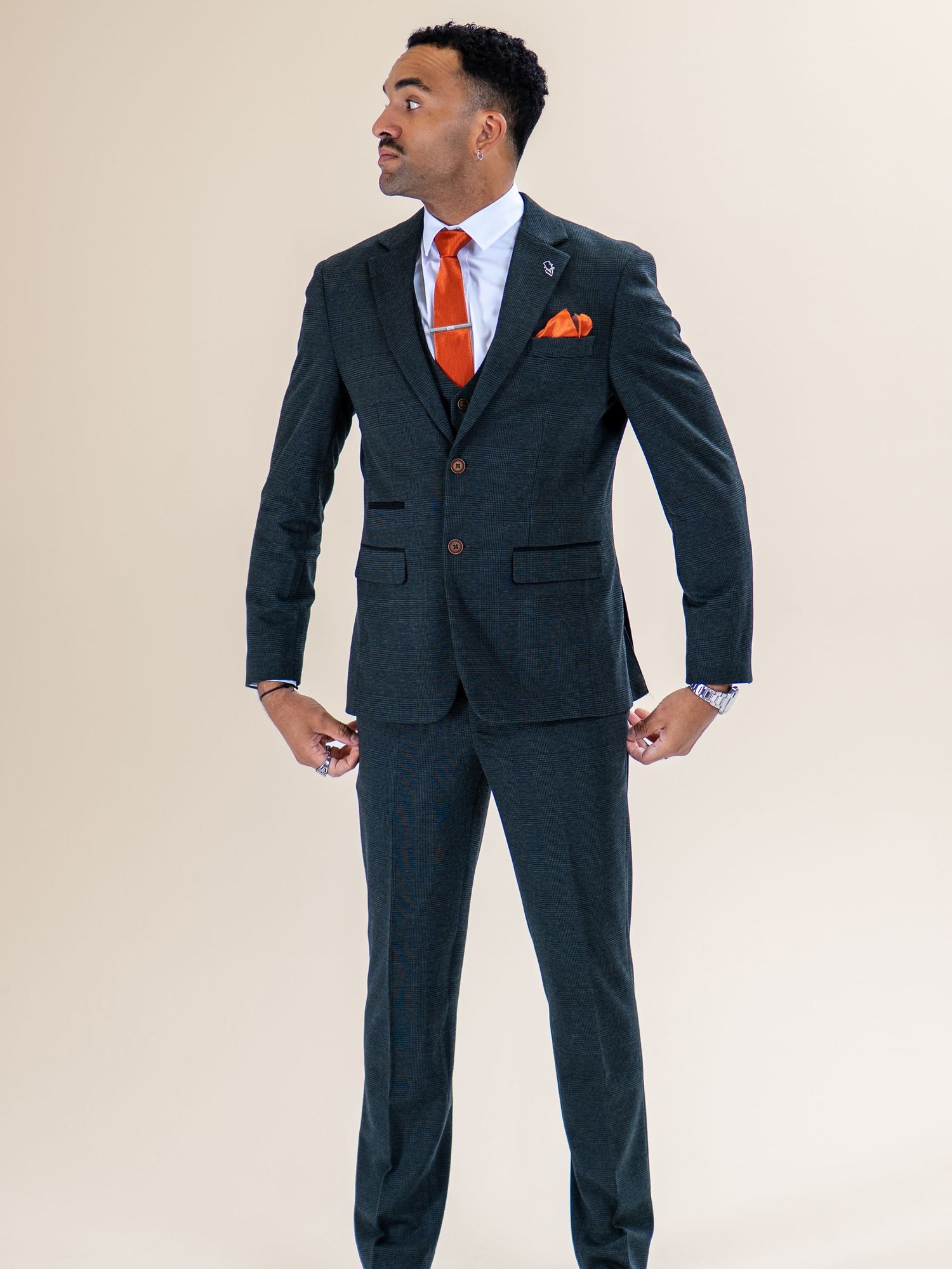 Man wearing a dark three-piece suit with an orange tie and pocket square in a studio setting.