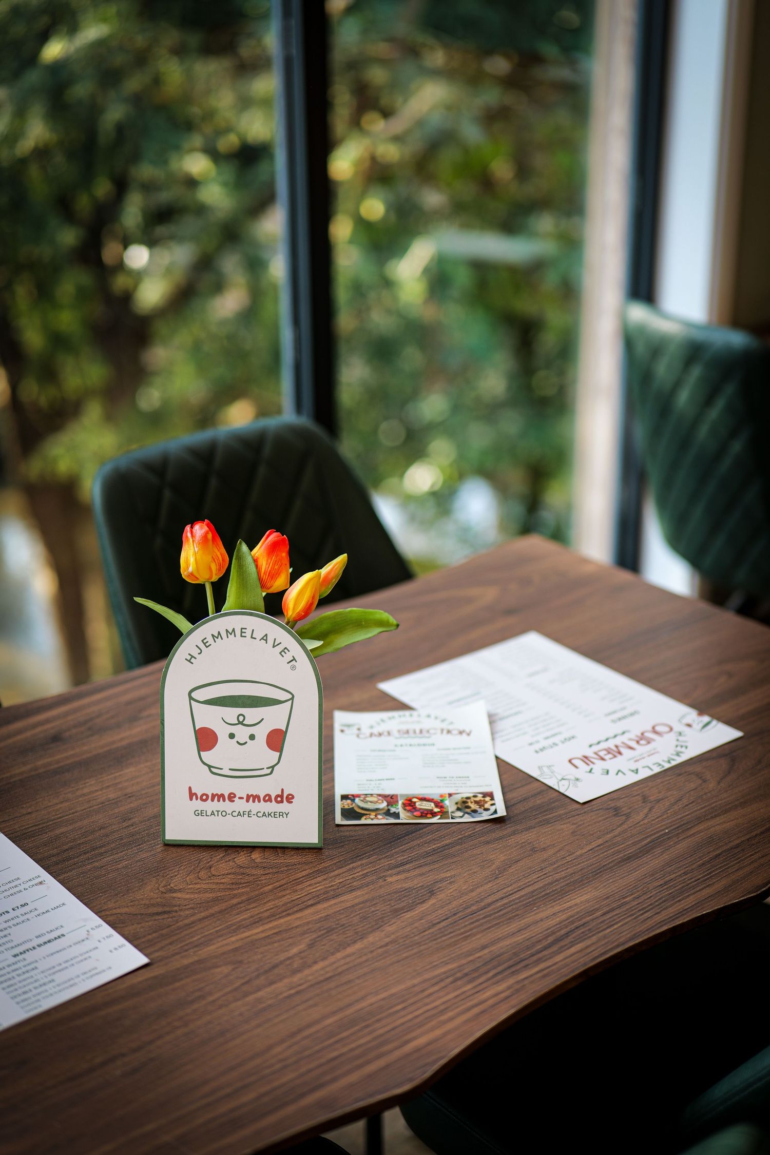 Cafe table with tulips in a vase, menus, and a home-made gelato cafe candy sign by a window.