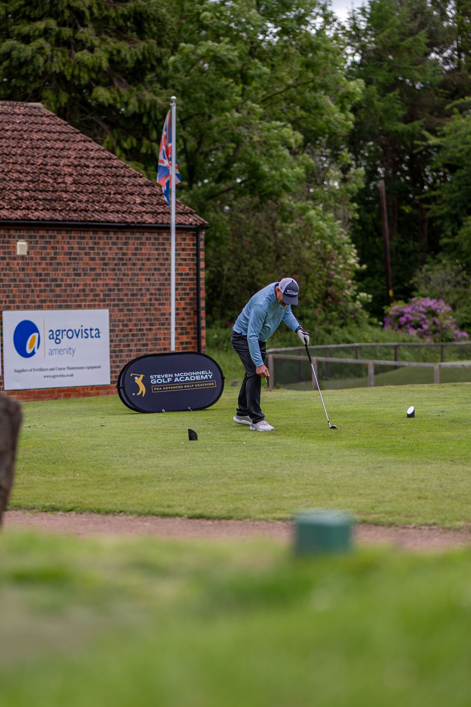 Golfer putting on a green near an Agrovista Energy banner and brick building.