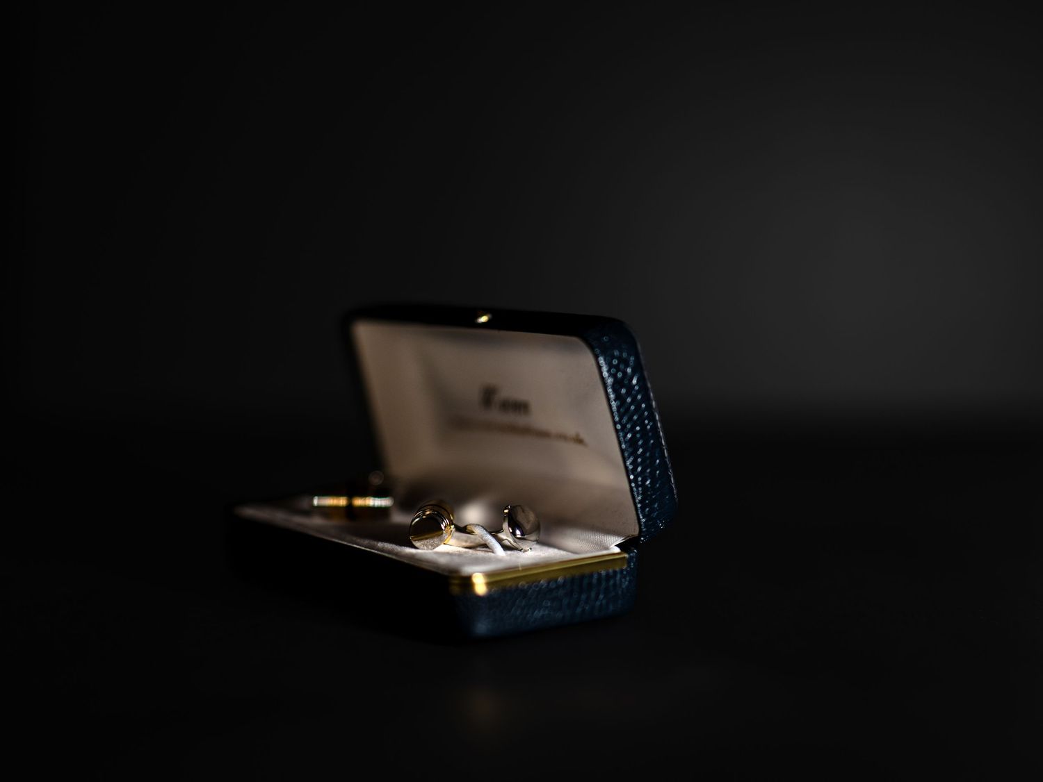 Gold cufflinks presented in open blue leather jewelry box on dark background.