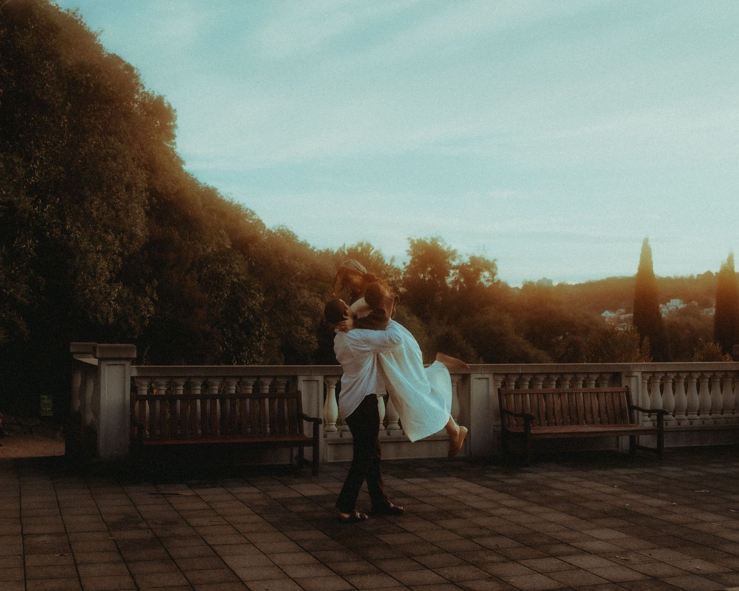 Groom lifting bride in a romantic embrace on a terrace at golden sunset.