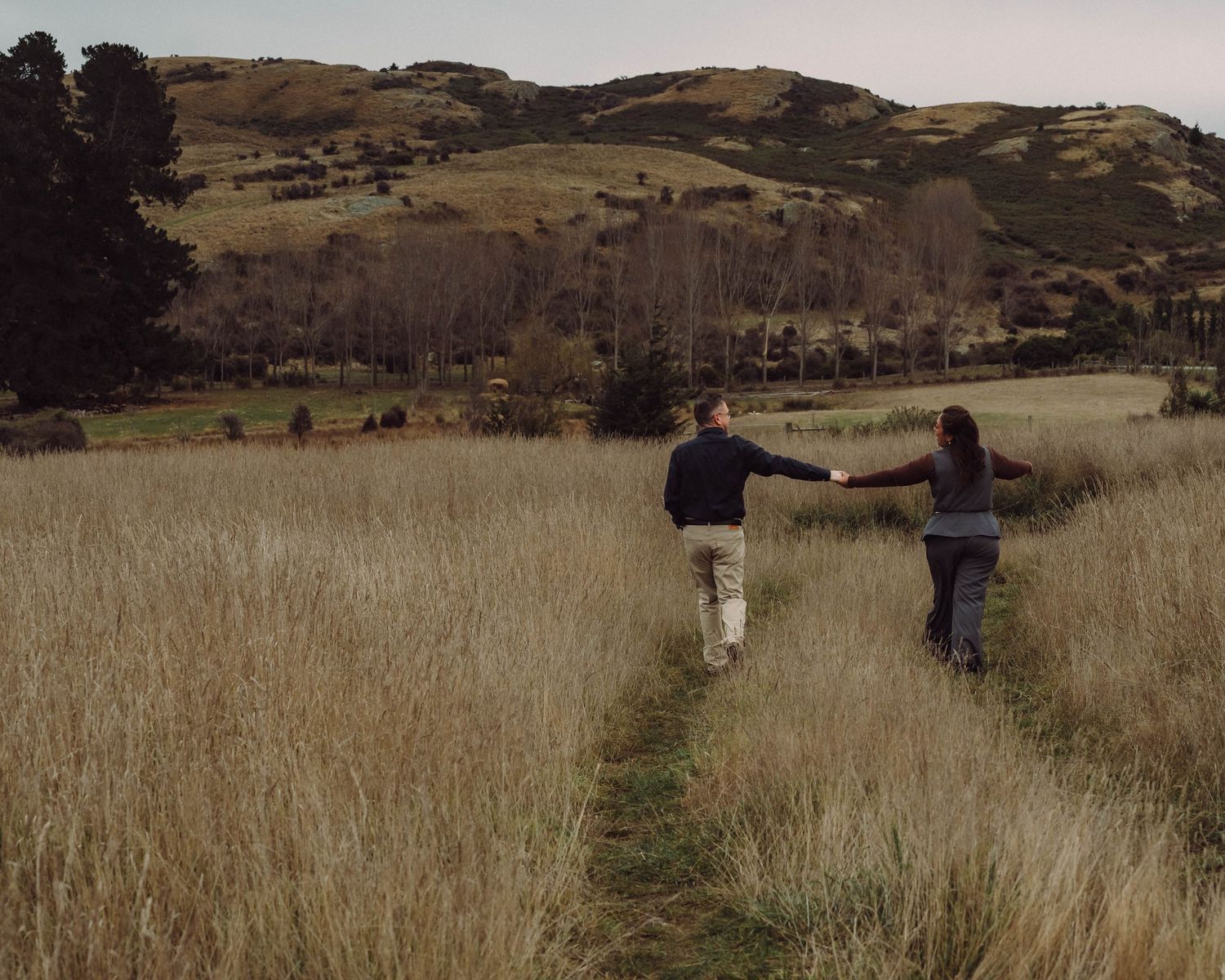 Couple holding hands walking down grassy path
