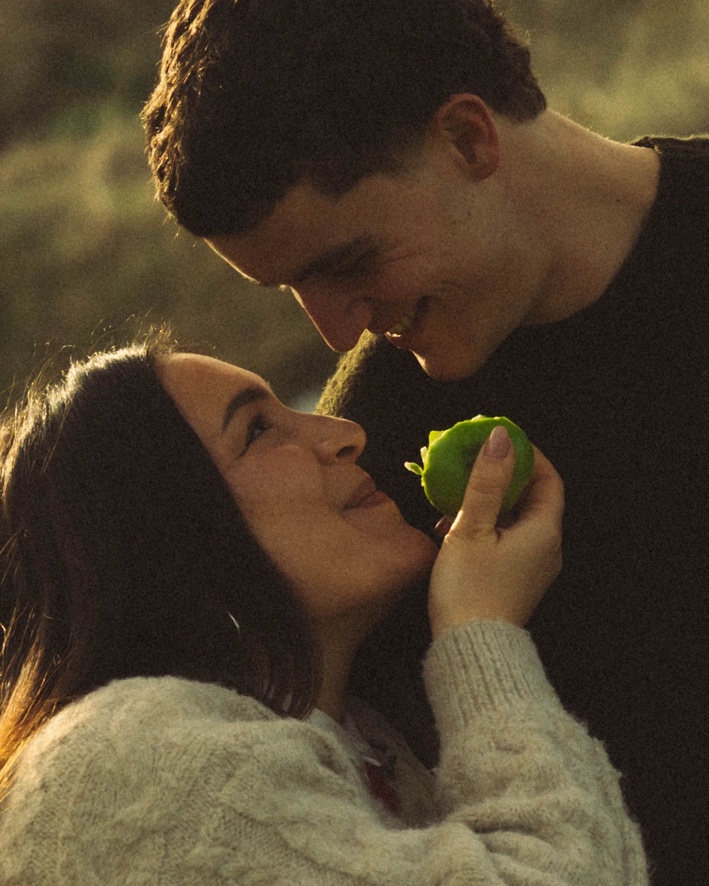 Romantic couple sharing tender moment holding a green apple in warm light.