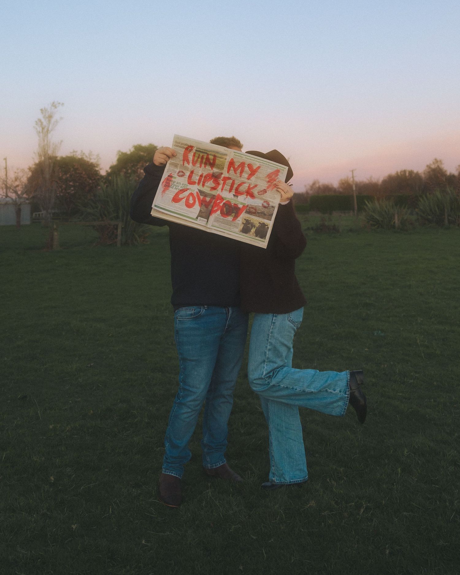Couple holding up newspaper that says 'Ruin my lipstick cowboy'