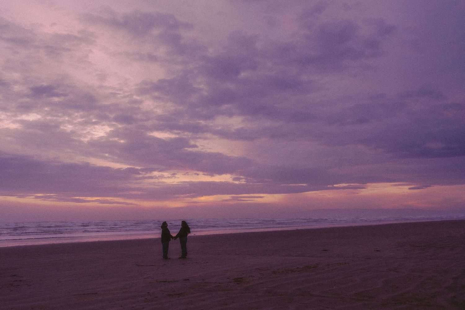 Silhouette of couple holding hands on a beach during a stunning purple and pink sunset. Located in Southland, New Zealand