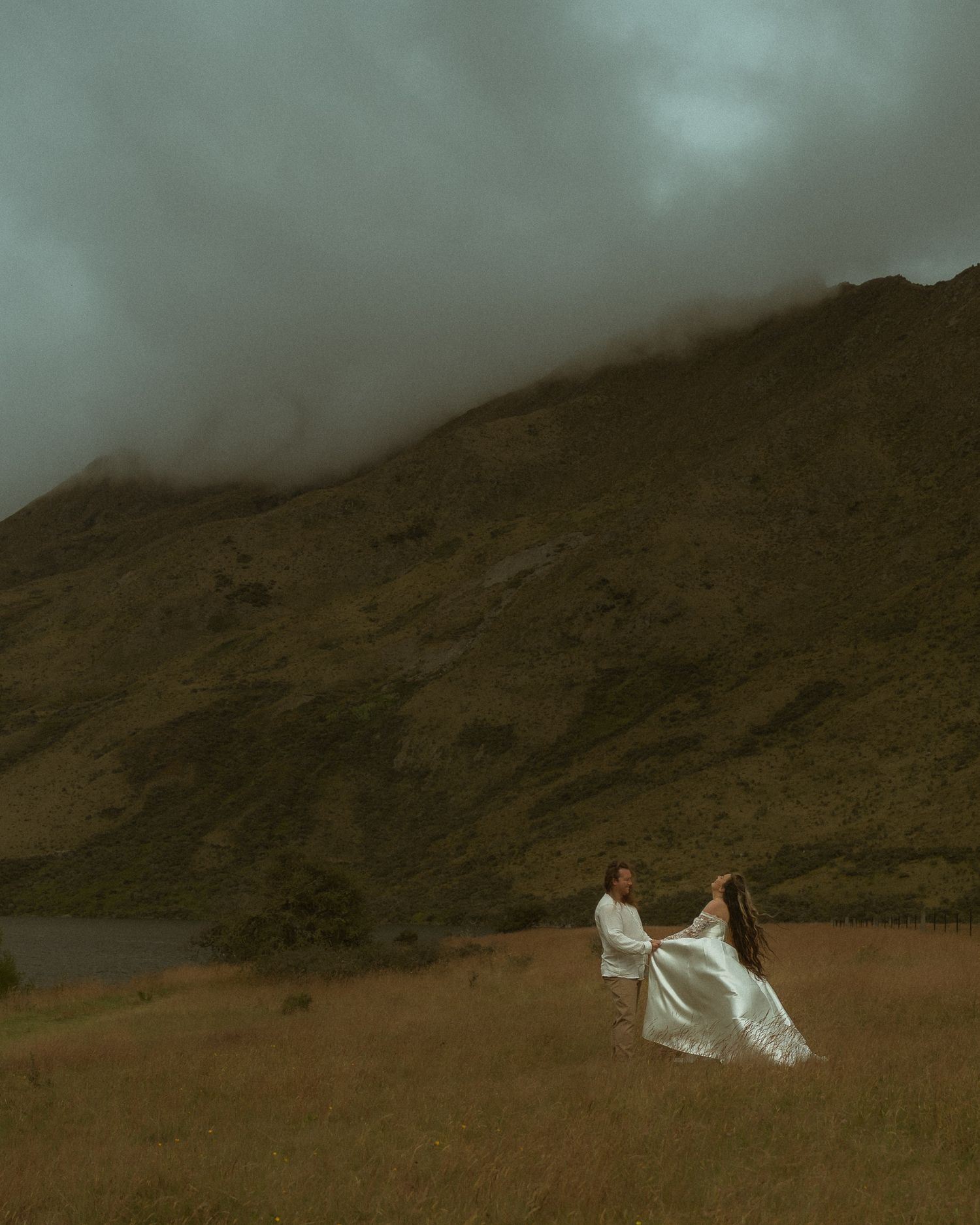Bride and groom dancing in a dramatic misty mountain landscape with stormy skies.