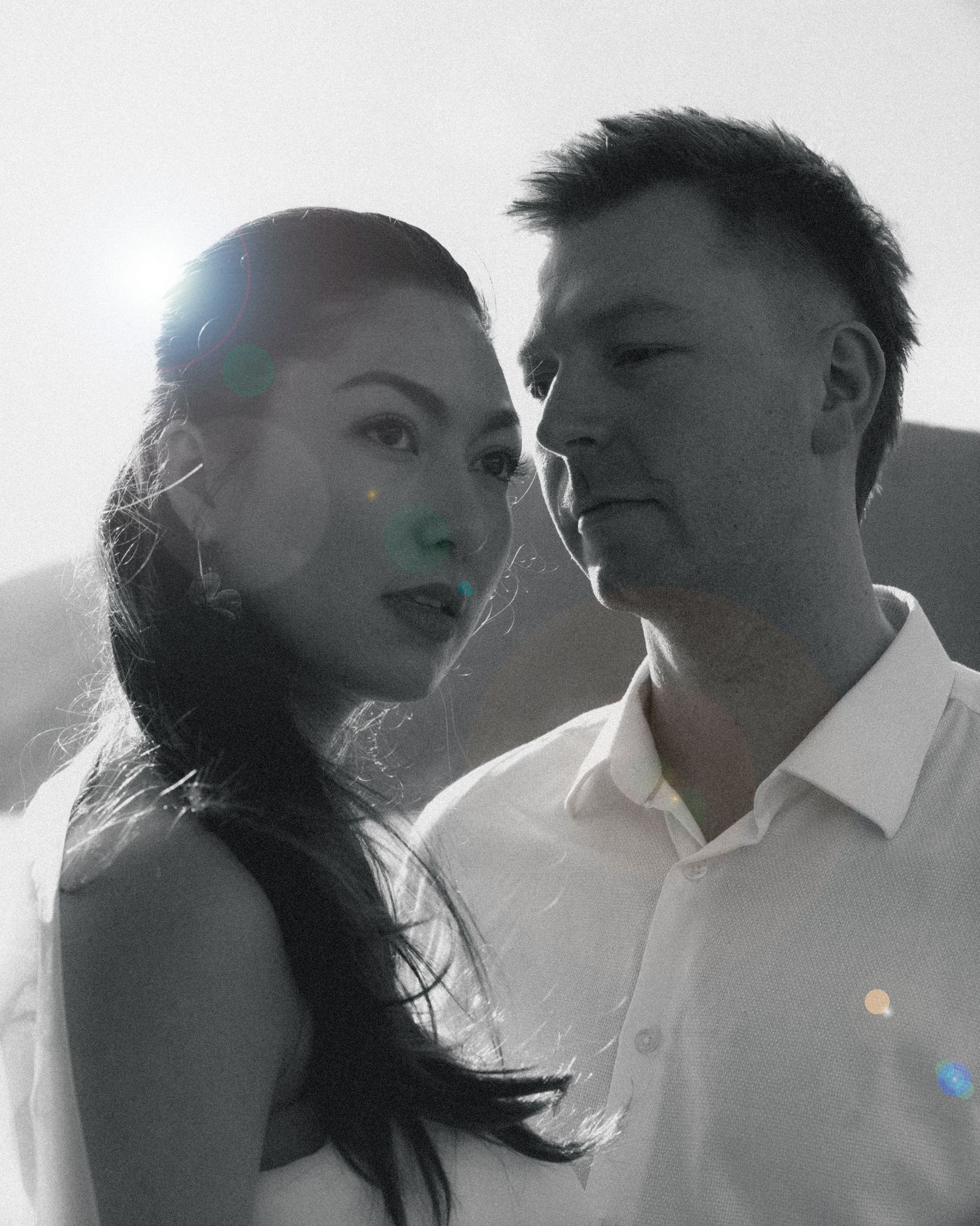 Stylish couple portrait with sun flare in a high-contrast black and white outdoor setting.