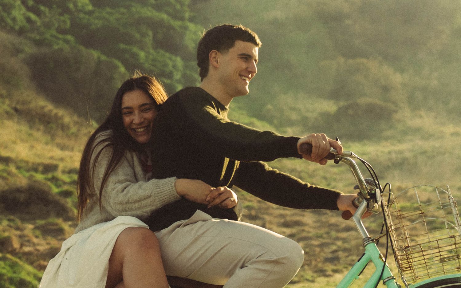 Joyful couple riding vintage bicycle together through lush green hillside.
