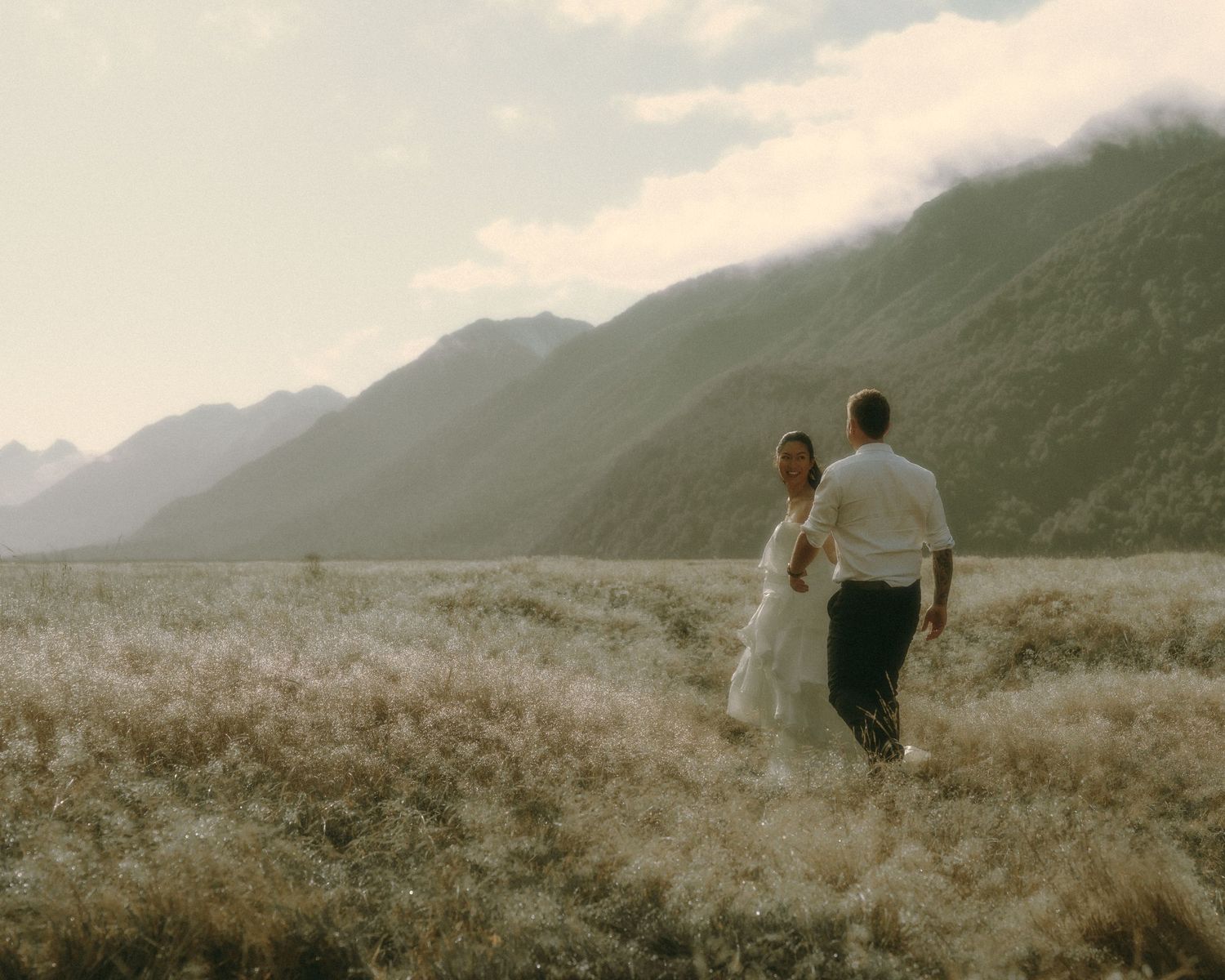 Wedding couple holding hands in mountain landscape.