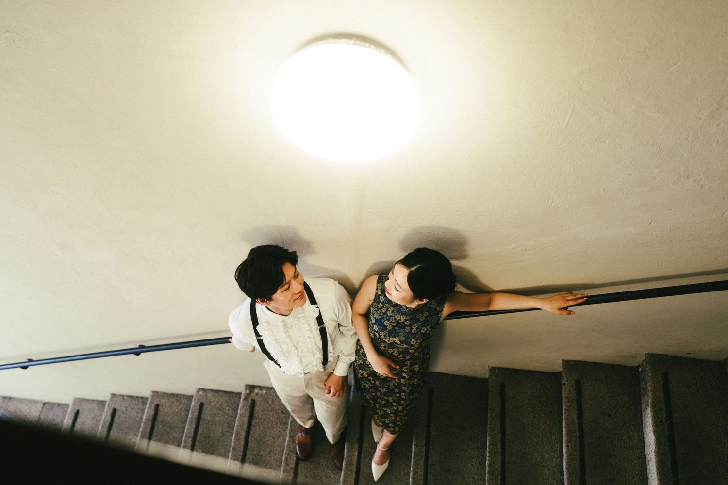 Aerial view of Asian couple smiling at each other on a staircase under round ceiling light.