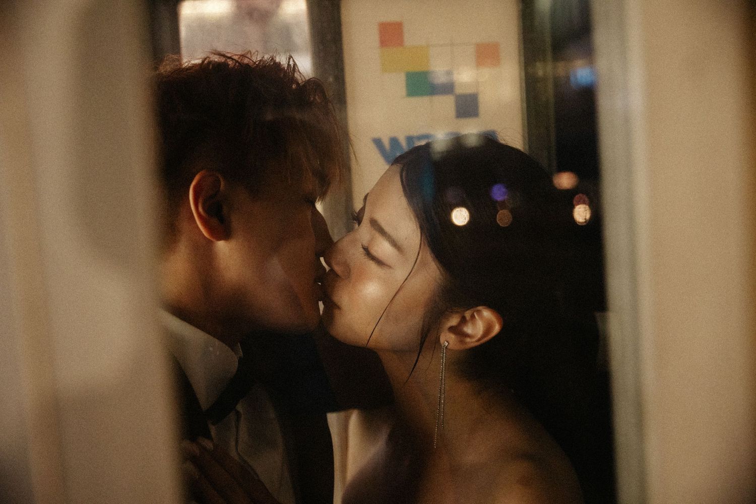 A couple shares a passionate kiss in a dimly lit urban setting at night.