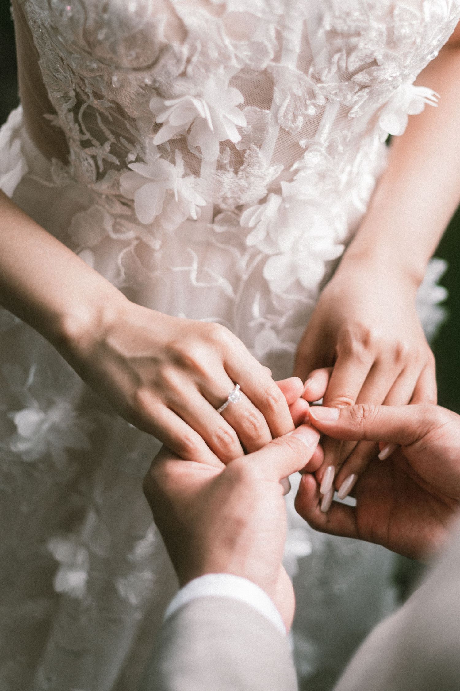 Close-up of bride and groom exchanging wedding rings, bride wearing floral lace wedding dress.
