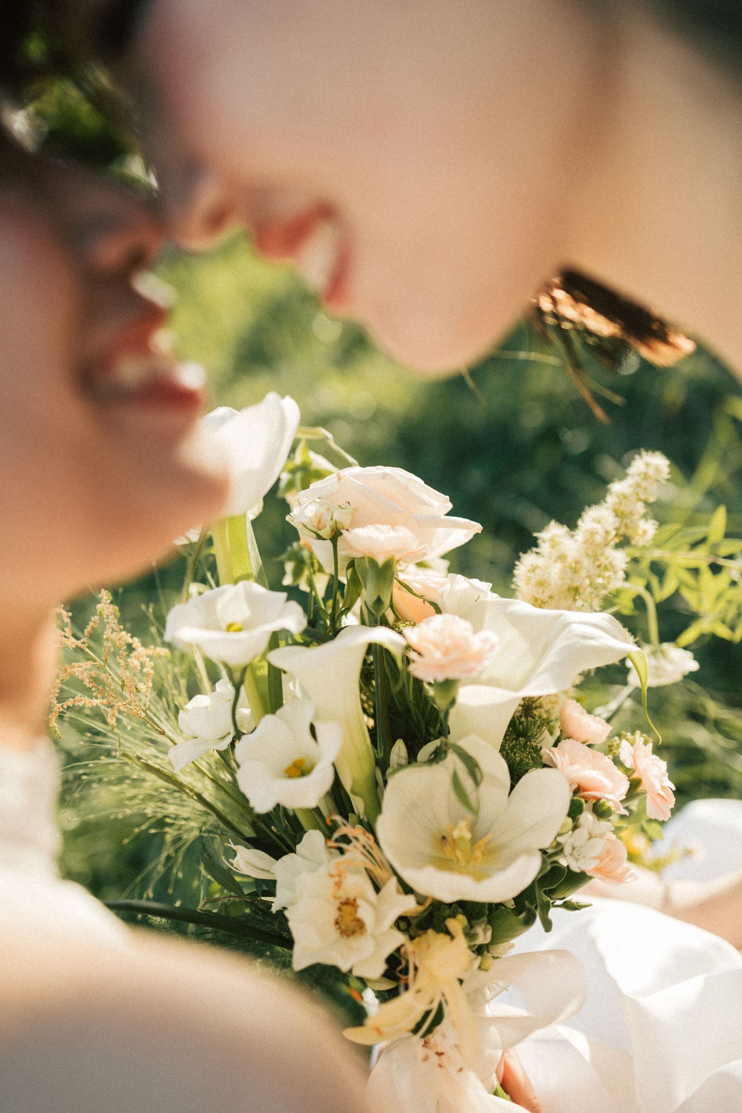 Smiling bride holding a beautiful bouquet of white and blush flowers in soft sunlight.