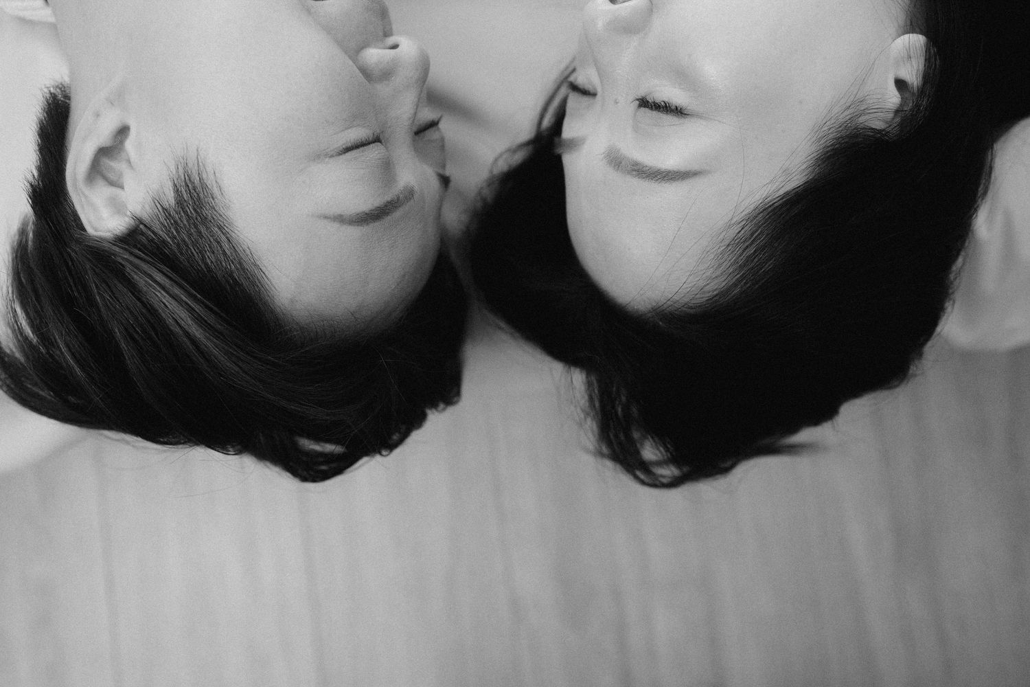 Black and white overhead view of two people lying head-to-head on a wooden floor smiling.