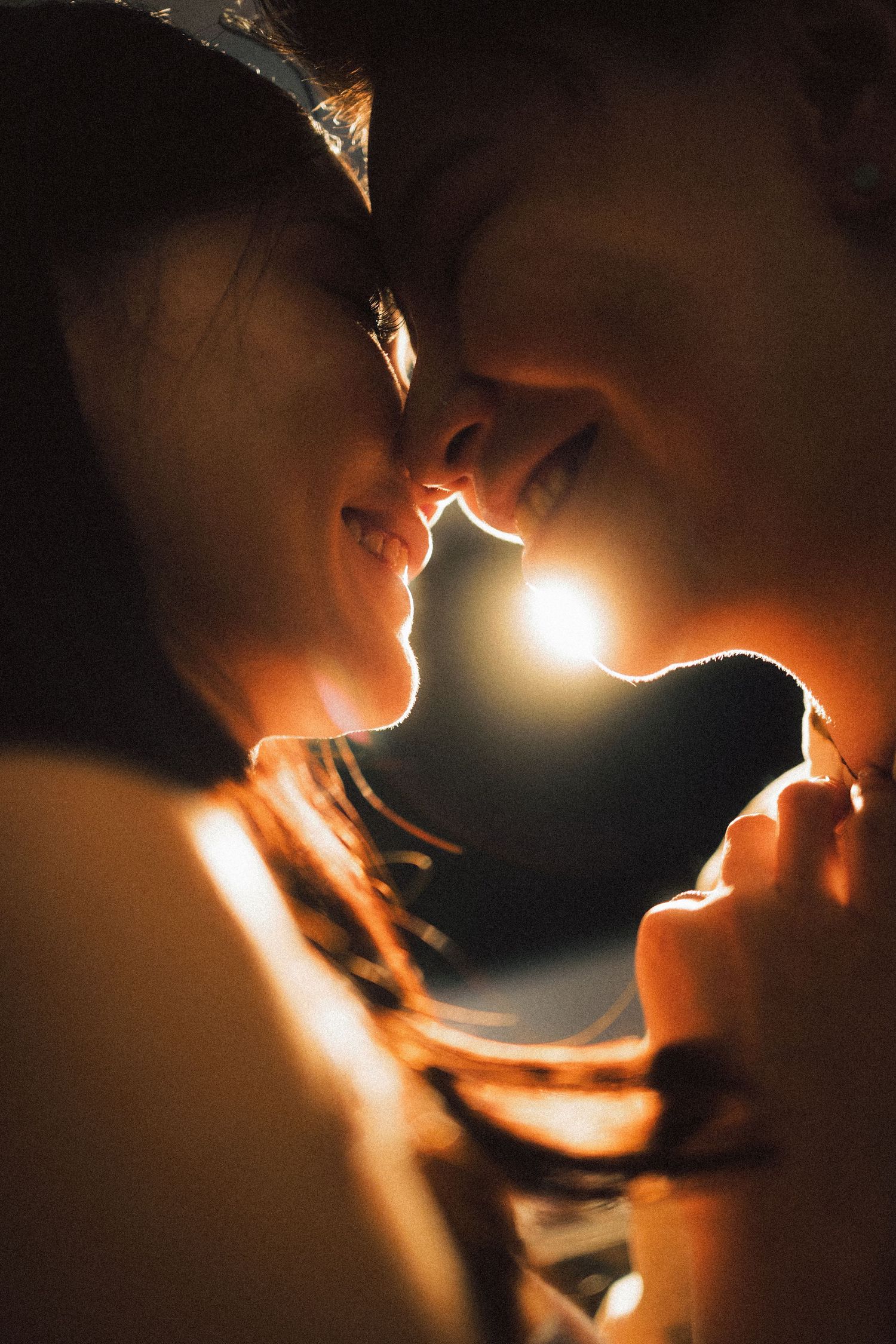 Romantic close-up of two people facing each other with warm golden backlight glowing.